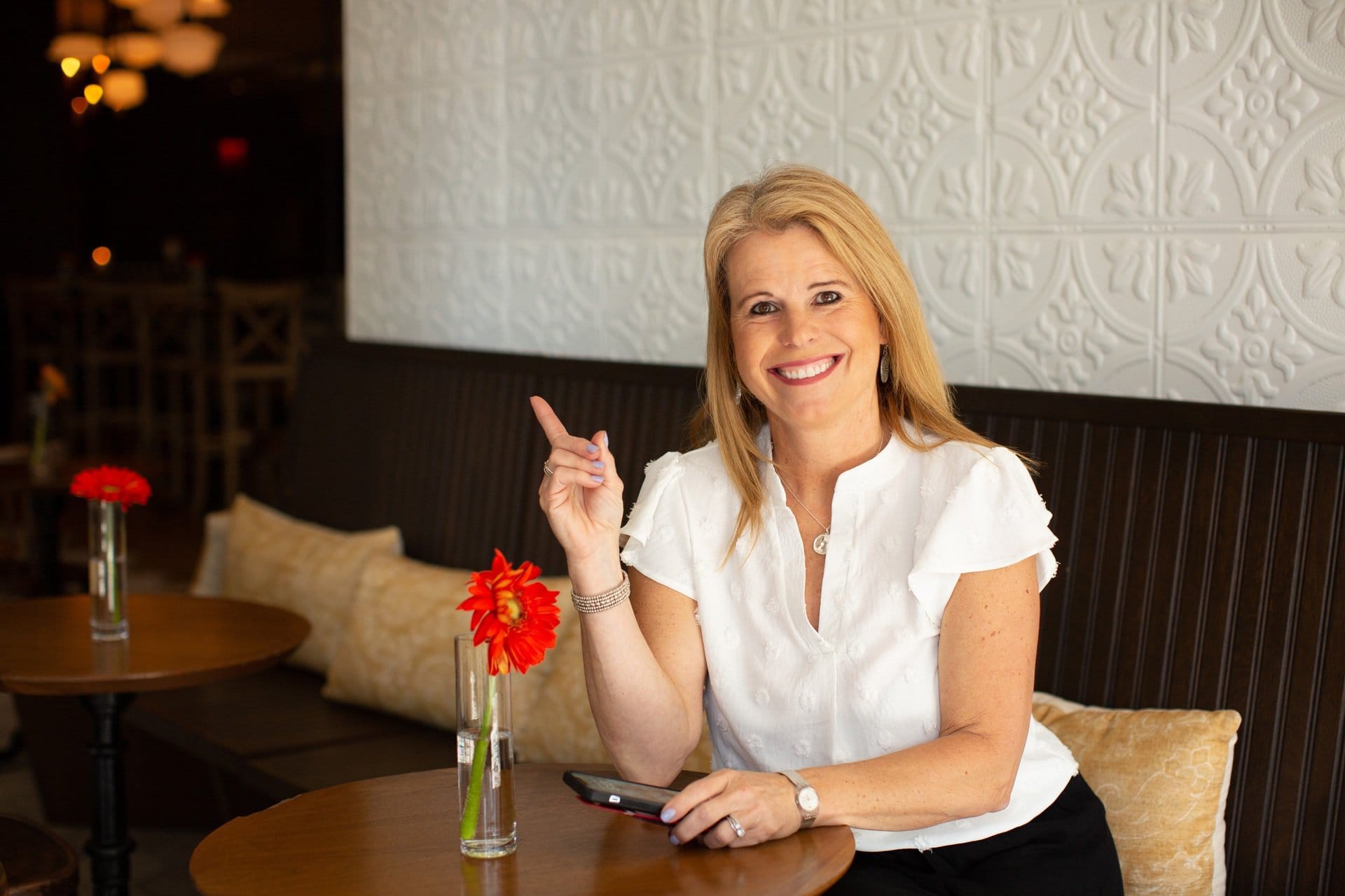 Laura Nelson sitting at a coffee shop table, holding a mobile phone, while smiling and pointing upwards